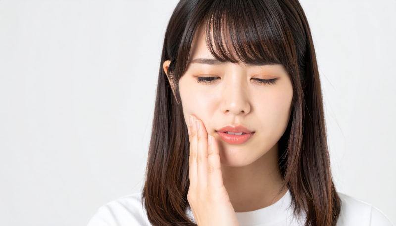 親知らずが生えて痛む頬をおさえる女性